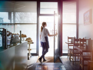 Image of a woman opening the door of a cafe she works at